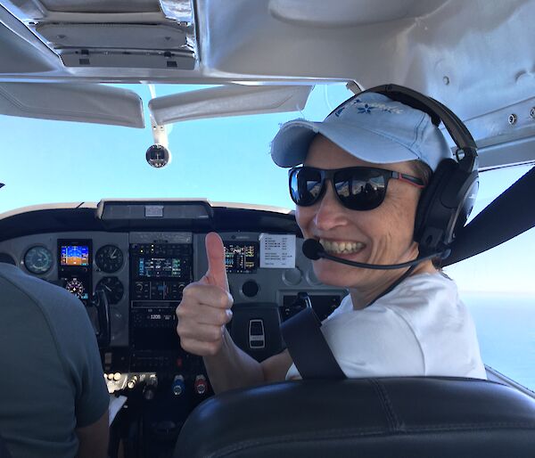 A woman smiles from the cockpit of a small plane