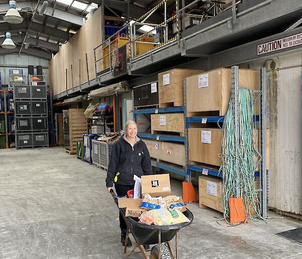 A women pushes a wheelbarrow full of food products through a warehouse