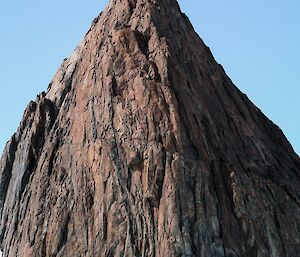 Three people stand dwarfed at base of large triangular rocky peak