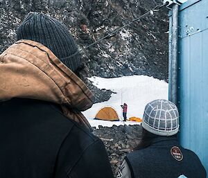 Shot taken  looking over the shoulders of two people as they watch another erect a tent