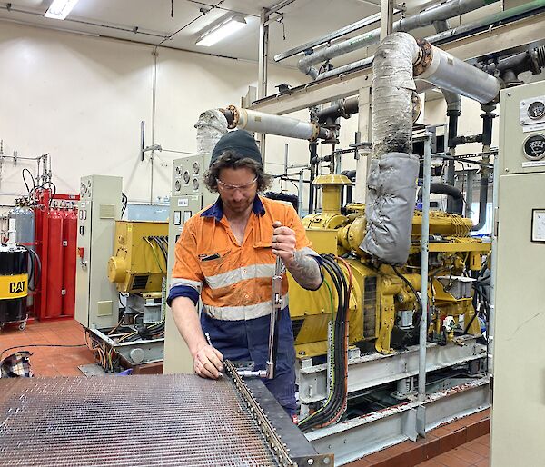 Man stands at workbench in powerhouse, adjusting bolts on generator filter