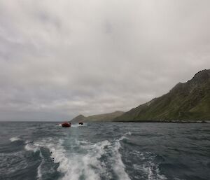 Two rubber boats cruise through the grey weather past the green slopes of the sland