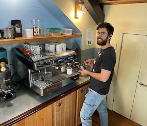 A smiling man standing at a large silver coffee machine making a coffee