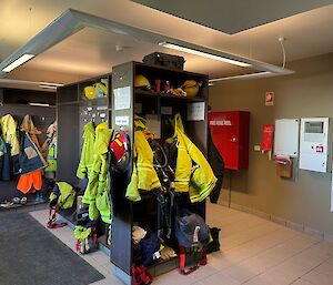 A small, tiled room with lots of coat hooks and shelves on which are hanging jackets including fire-fighters bright yellow jackets.