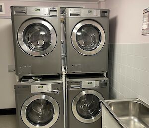 Four shiny silver washing machines in a laundry stacked two apiece.