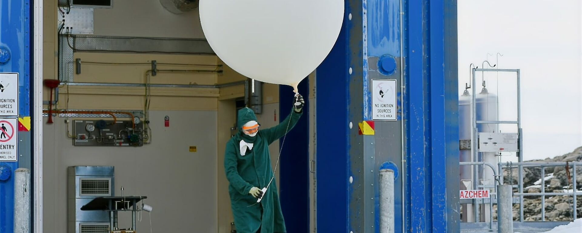 Meteorlogy observer in PPE walking out of balloon shed with weather balloon