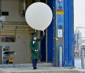 Meteorlogy observer in PPE walking out of balloon shed with weather balloon
