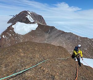 Rocky peak in foreground with climber preparing to abseil down, with ridge line of David Ranges in distance