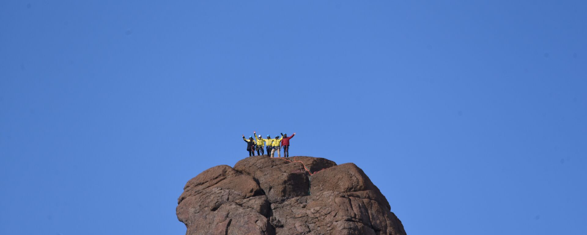 The peak of Fang Mountain in the distance, with five people on summit waving to camera