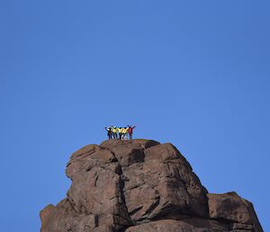 The peak of Fang Mountain in the distance, with five people on summit waving to camera