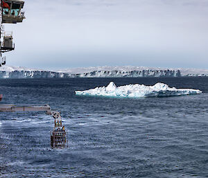 A water sampling instrument being lowered from the side of a ship, with icebergs in the distance.