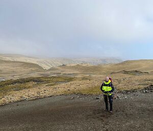 A man standing on a rocky shore with misty mountains behind.