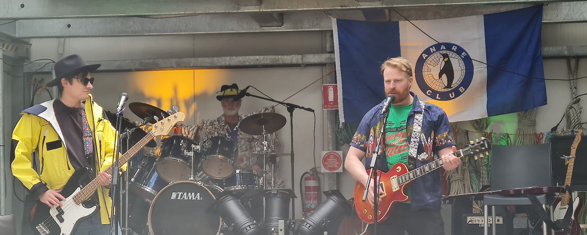 Two base guitarists and a drummer on a stage playing music.