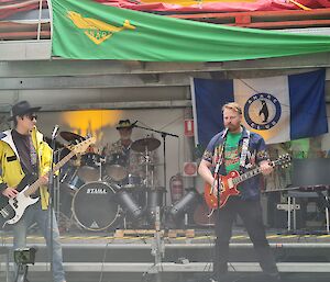 Two base guitarists and a drummer on a stage playing music.