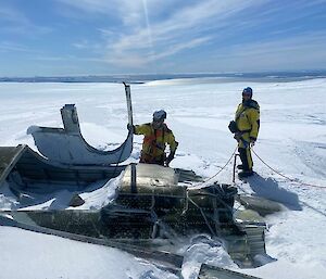 Men in harnesses and safety helmets, stand beside fuselage of aircraft which is mostly covered in ice