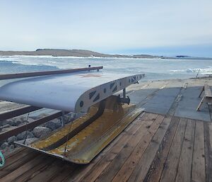 Piece of aircraft wing made into a picnic table, sits on wooden decking with ice covered harbour in background