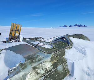 Fuselage of aircraft which is mostly covered in ice in foreground with ice plateau and mountain peaks on horizen