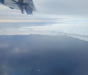 View from plane window of ocean with iceberg floating and plane wing