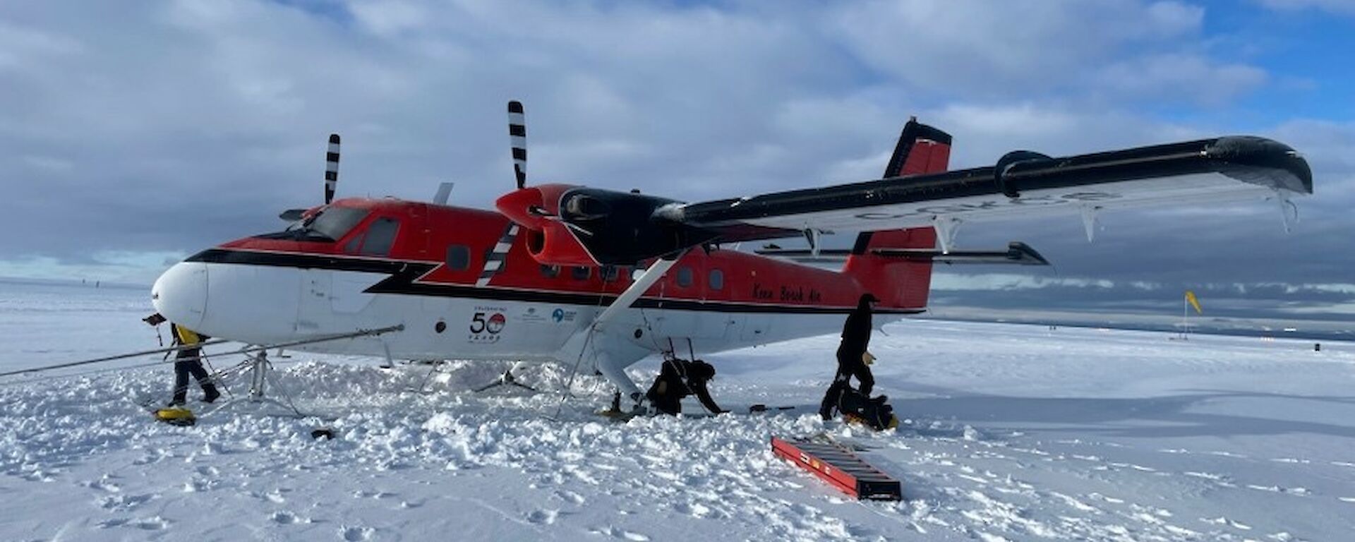 A red and white Twin Otter aircraft with skis parked on the ice.