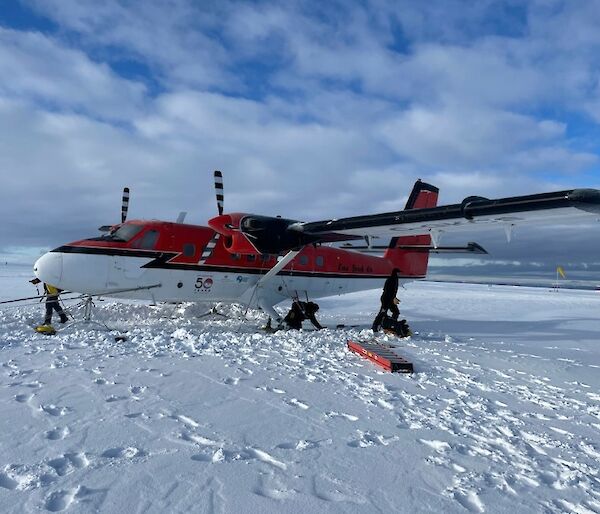 A red and white Twin Otter aircraft with skis parked on the ice.