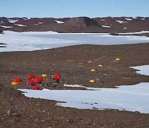 A scattering of red huts and yellow tents on a rocky field, with snow and mountains in the background.