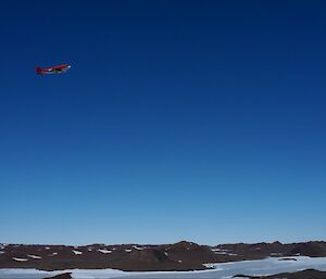 A red Basler aircraft flying over rocky mountains against a cloudless blue sky.