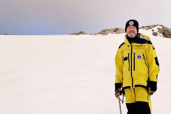 A man in yellow cold weather gear stands on snow
