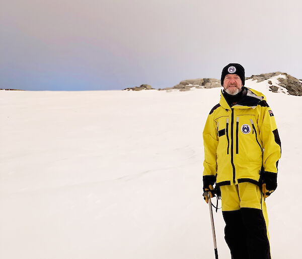 A man in yellow cold weather gear stands on snow