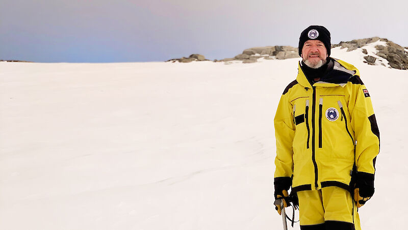 A man in yellow cold weather gear stands on snow