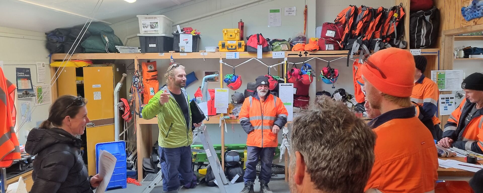 A group of people in a warehouse are taught how to use safety gear