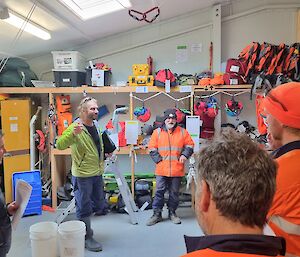 A group of people in a warehouse are taught how to use safety gear