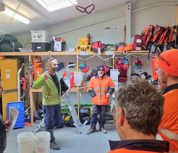 A group of people in a warehouse are taught how to use safety gear