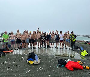 A group of people in swimming gear stand in the cold on a grey day
