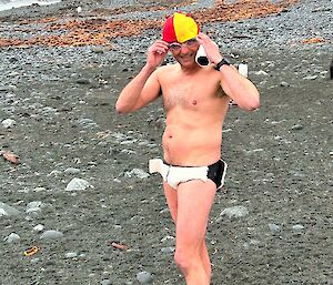 A man prepares for a swim dressed in swimming gear with a yellow and red lifeguard cap