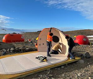 3 people work to install a hut in an ice free area in Antarctica