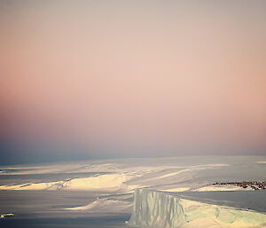Icebergs sit quietly under a large pink sky