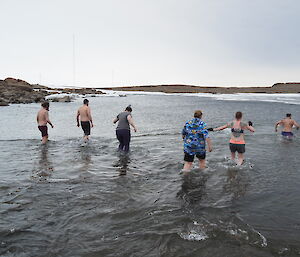 A group of swimmers enter the water with sea ice present across the bay
