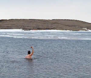 A sole swimmer raises an arm in the icy cold waters of Antarctica