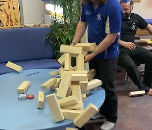 Two people laugh as a wooden tower crashes from the table