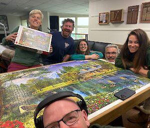 Group of smiling people around a table having completed a jigsaw puzzle.