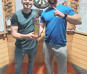 Two darts players posing for a photo in front of a darts board.