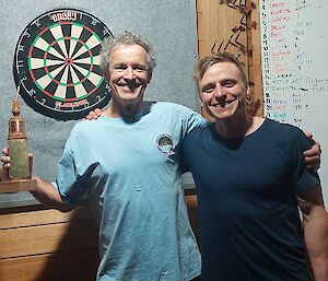 Two darts players standing in front of a dart board.