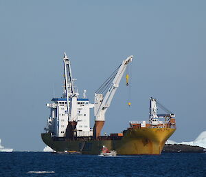 A small barge next to a very large yellow cargo ship with ice-bergs in the background.