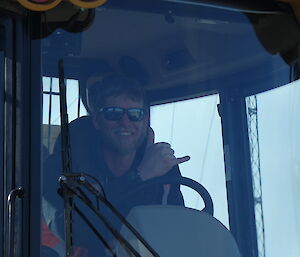 A smiling man in a big yellow truck gives the "it's all cool" gesture from behind the steering wheel.