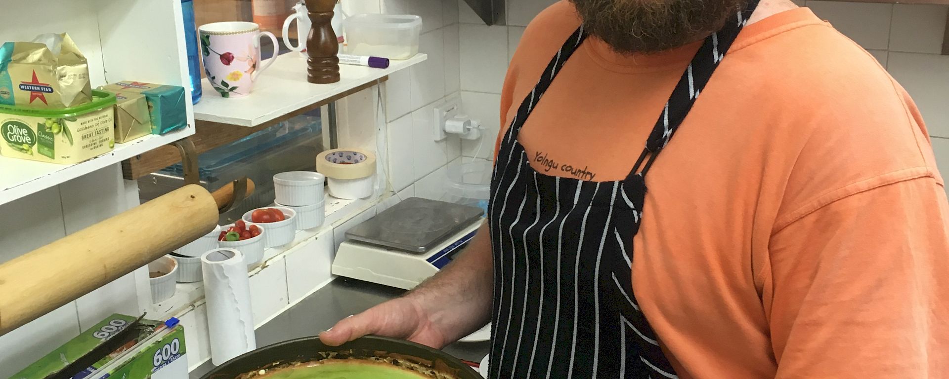 A smiling bearded man holds a green cake in a kitchen