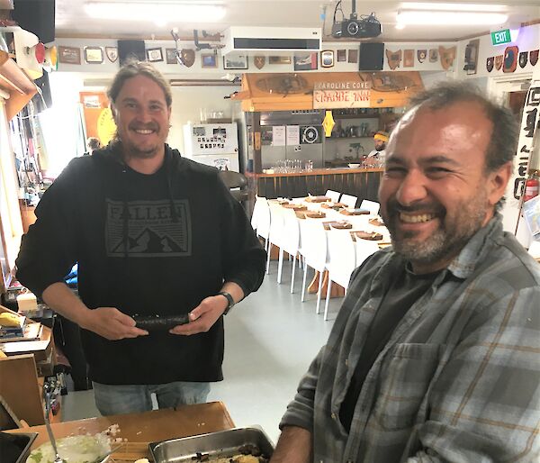 Two smiling men prepare sushi in a large kitchen