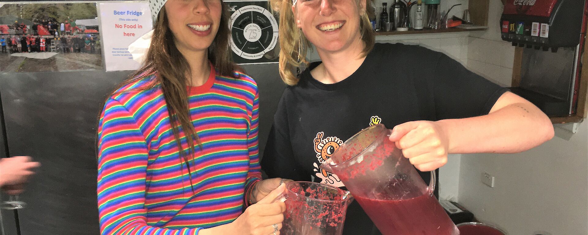 Two ladies prepare large jugs of a red drink