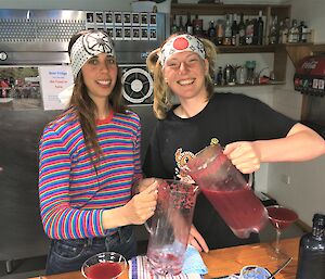 Two ladies prepare large jugs of a red drink