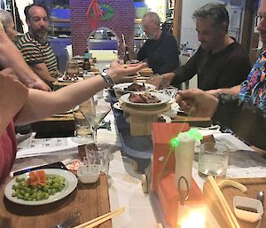A group of people sit around a table with lots of Japanese food on offer.