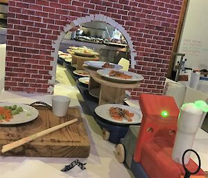 A toy train delivers food on a table after coming through a hand made archway